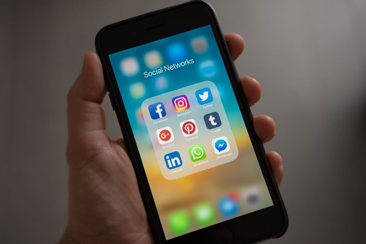 Hand holding a smartphone showing a folder of social media apps