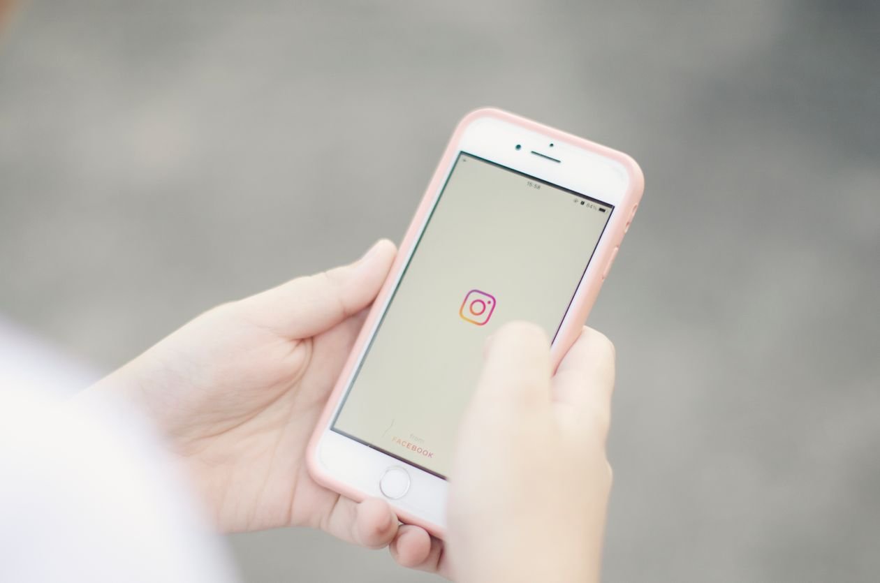 Hands holding a smartphone with the Instagram feed open, checking the app before posting