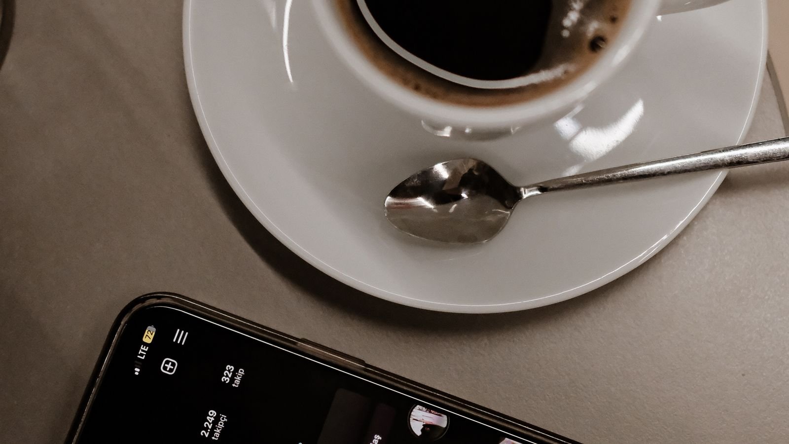 A cup of black coffee next to a smartphone showing a social media app on a cafe table