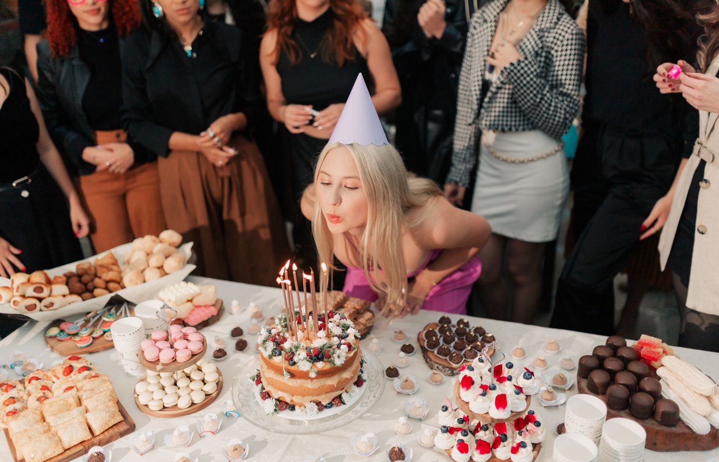 Young woman celebrating her birthday with friends around a table of cakes and desserts